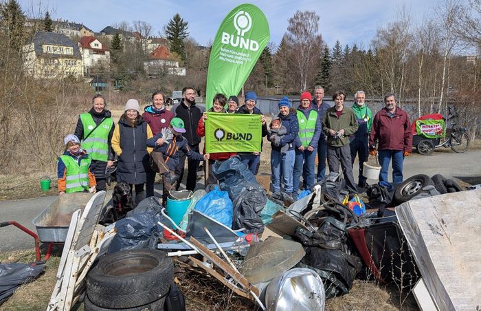 Sechzehn Menschen stehen vor einem großen Haufen Müll, den sie gesammelt haben