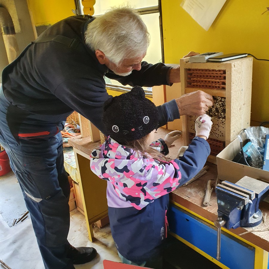 Ein älterer Mann und ein kleines Mädchen schlichten trockene Halmstücke in einen Holzkasten