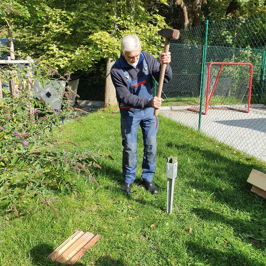 Ein älterer Mann schlägt mit einem Vorschlaghammer eine Stahlhülse in die Erde