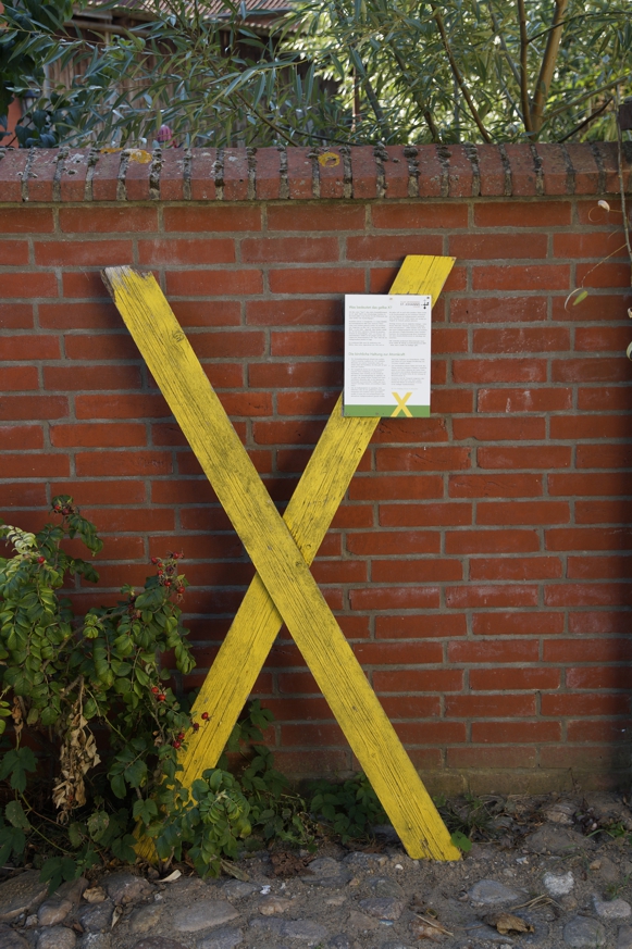 Ein gelbes Kreuz - Zeichen des Bürgerprotestes - lehnt an einer Kirchhofsmauer